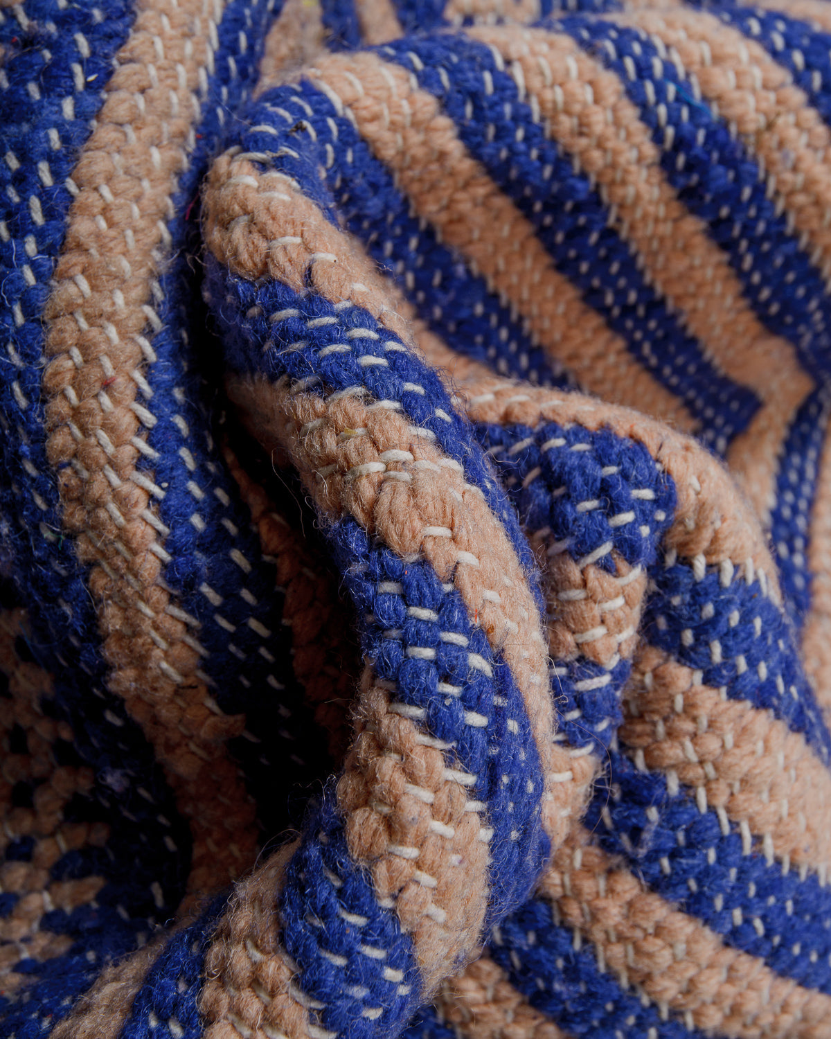 Close-up of blue and rose coloured kelim with white cotton stitching.